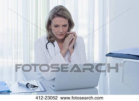 Female doctor sitting at desk with laptop in office View Large Photo Image Stock Image - Female doctor sitting at desk with laptop in office. Fotosearch