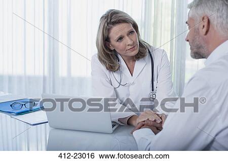 Female doctor sitting at desk with laptop and consoling patient View Large Photo Image Stock Photograph - Female doctor sitting at desk with laptop and consoling patient. Fotosearch