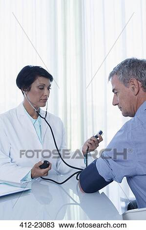 Female doctor taking patient's blood pressure at desk in office View Large Photo Image Stock Image - Female doctor taking patient's blood pressure at desk in office. Fotosearch