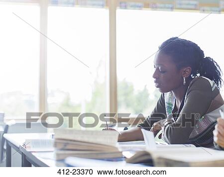 Stock Image - Female student writing at desk in classroom. Fotosearch