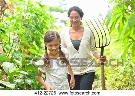 Girl and woman with gardening fork walking through plants in greenhouse View Large Photo Image Stock Photograph - Girl and woman with gardening fork walking through plants in greenhouse. Fotosearch