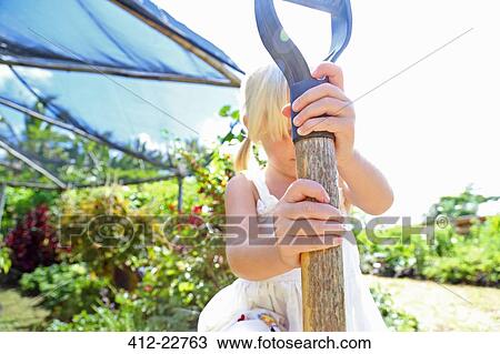 Stock Image - Girl holding shovel in sunny garden. Fotosearch