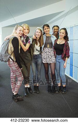 Stock Image - Group portrait of cheerful female students standing in locker room. Fotosearch