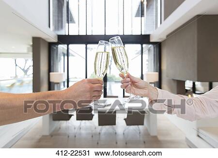 Hands of couple raising toast with champagne flutes in modern dining room View Large Photo Image Stock Image - Hands of couple raising toast with champagne flutes in modern dining room. Fotosearch