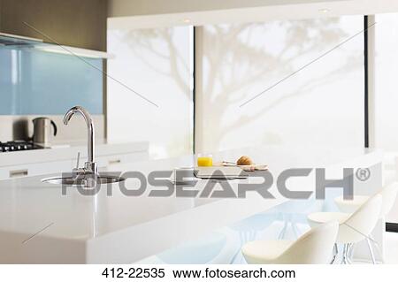 Stock Photography - Laptop, coffee cup, glass of juice, croissant and newspaper on modern kitchen counter. Fotosearch