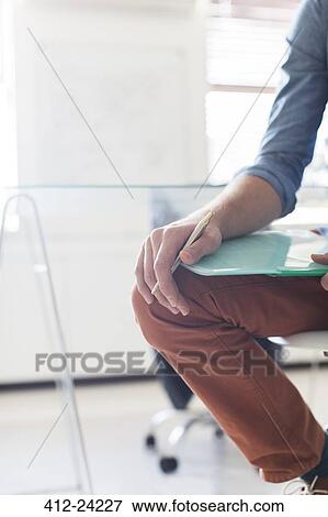 Stock Photo - Leg and hand of man holding documents and pen. Fotosearch