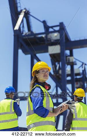 Stock Image - Low angle view of worker standing near cargo crane. Fotosearch