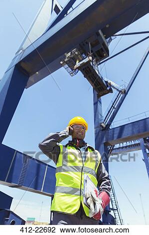Low angle view of worker talking on walkie-talkie under cargo crane View Large Photo Image Stock Image - Low angle view of worker talking on walkie-talkie under cargo crane. Fotosearch