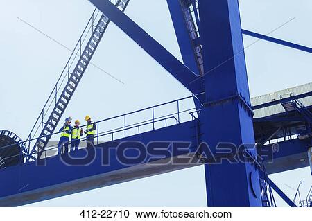 Stock Image - Low angle view of workers on cargo crane. Fotosearch