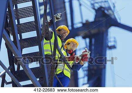 Stock Image - Low angle view of workers standing on cargo crane. Fotosearch