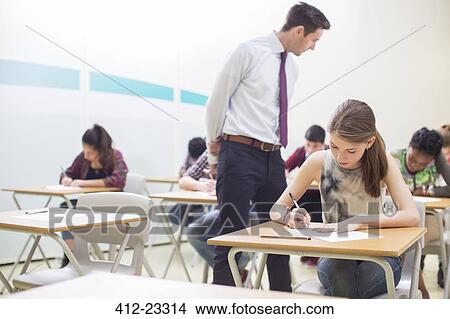 Picture - Male teacher supervising students writing their GCSE exam in classroom. Fotosearch