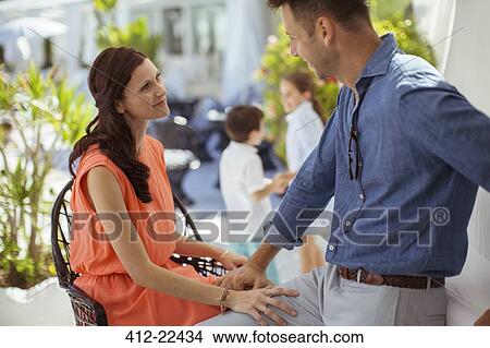 Man and woman sitting face to face outdoors, children in background View Large Photo Image Picture - Man and woman sitting face to face outdoors, children in background. Fotosearch