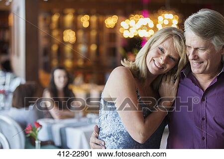 Stock Image - Man embracing woman in restaurant, people in background. Fotosearch