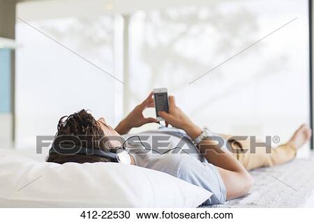 Man listening to music while lying on bed View Large Photo Image Stock Image - Man listening to music while lying on bed. Fotosearch