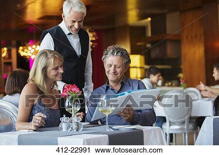 Stock Image - Man ordering meal at fancy restaurant table, waiter standing behind. Fotosearch