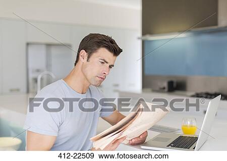 Man reading newspaper in modern kitchen, laptop and orange juice on counter View Large Photo Image Stock Photo - Man reading newspaper in modern kitchen, laptop and orange juice on counter. Fotosearch