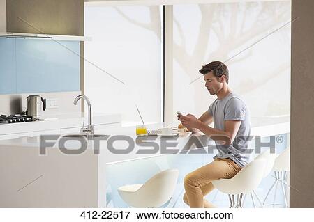 Man sitting on stool at kitchen island and using phone View Large Photo Image Stock Photo - Man sitting on stool at kitchen island and using phone. Fotosearch