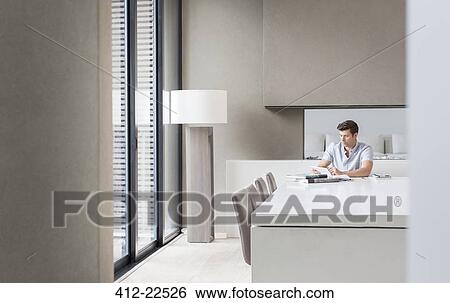 Stock Photograph - Man using tablet pc in modern dining room. Fotosearch
