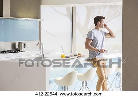Man with coffee cup using phone in modern kitchen View Large Photo Image Picture - Man with coffee cup using phone in modern kitchen. Fotosearch