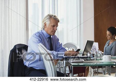 Stock Photograph - Mature business man using mobile phone at restaurant table, woman in background. Fotosearch