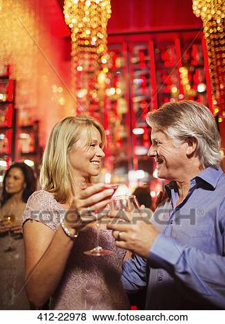 Stock Photo - Mature couple standing face to face and holding drinks in nightclub. Fotosearch
