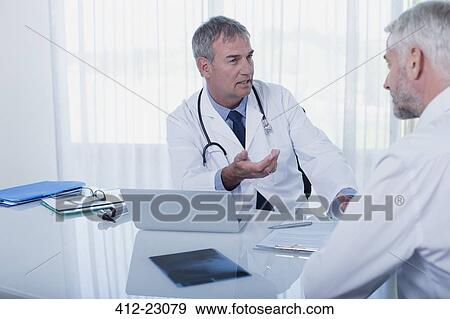 Stock Photo - Mature doctor talking to patient at desk in office. Fotosearch