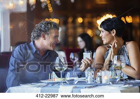 Stock Photo - Mature man giving gift to smiling woman in restaurant. Fotosearch