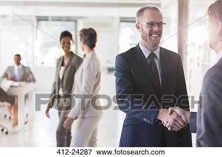 Men shaking hands, colleagues in background View Large Photo Image Stock Photo - Men shaking hands, colleagues in background. Fotosearch