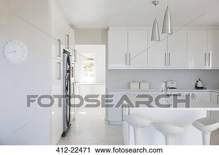 Stock Image - Modern white and clean kitchen interior with stools at counter. Fotosearch