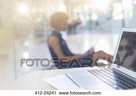 Stock Image - Open laptop on desk, woman in background. Fotosearch