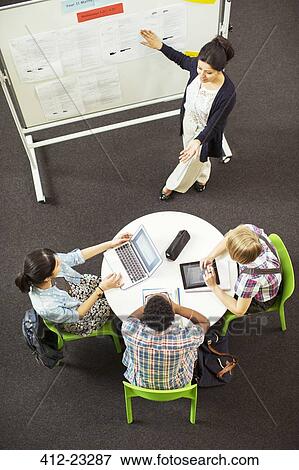 Stock Photo - Overhead view of student looking at teacher showing documents on whiteboard. Fotosearch