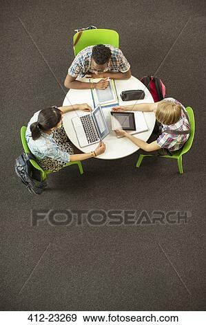 Stock Photo - Overhead view of students doing homework together, using laptop and digital tablet. Fotosearch