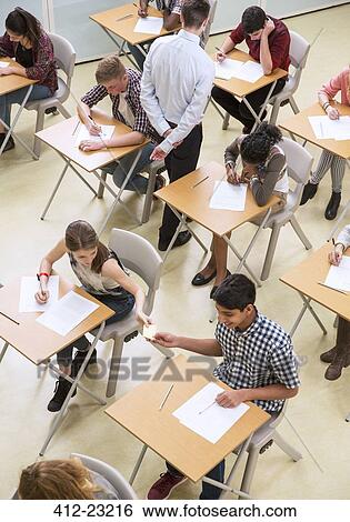 Stock Photograph - Overhead view of students passing note between desks during their GCSE exam . Fotosearch