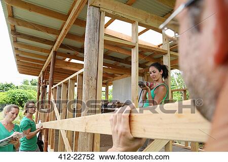Stock Image - People building wooden house frame together. Fotosearch