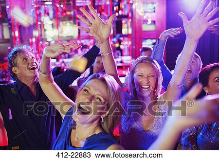 Stock Image - People raising hands and laughing in nightclub. Fotosearch
