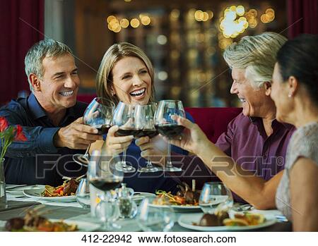 Stock Image - People toasting with red wine in restaurant. Fotosearch