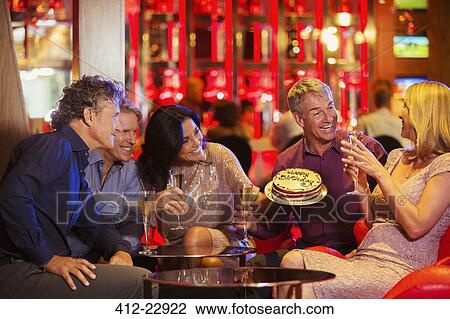 Stock Image - People with champagne flutes and birthday cake celebrating birthday in night club. Fotosearch