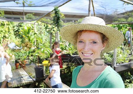 Portrait f smiling woman wearing sunhat in greenhouse, children in background View Large Photo Image Stock Image - Portrait f smiling woman wearing sunhat in greenhouse, children in background. Fotosearch