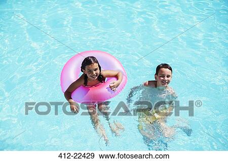Stock Photo - Portrait of brother and sister with pink inflatable ring in swimming pool. Fotosearch