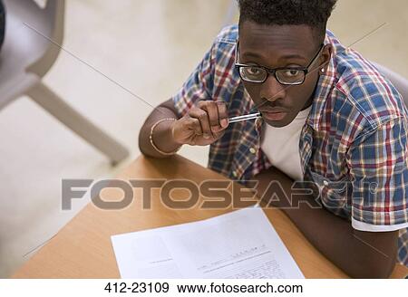 Portrait of male student wearing glasses sitting at desk in classroom View Large Photo Image Stock Photo - Portrait of male student wearing glasses sitting at desk in classroom. Fotosearch