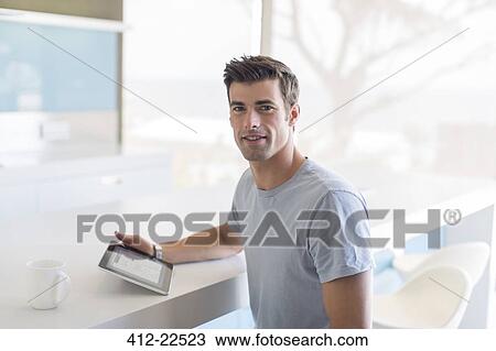 Stock Image - Portrait of man with tablet pc in kitchen. Fotosearch