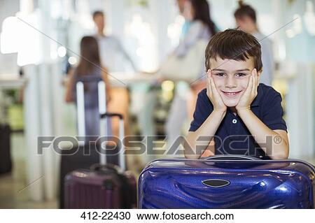 Stock Image - Portrait of smiling boy leaning on suitcase in hotel lobby. Fotosearch