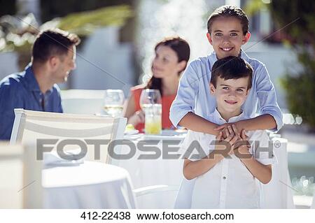 Portrait of smiling brother and sister, parents sitting at table in background View Large Photo Image Stock Photo - Portrait of smiling brother and sister, parents sitting at table in background. Fotosearch