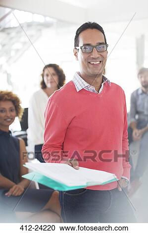 Portrait of smiling businessman wearing glasses and pink sweatshirt holding documents, office team in background View Large Photo Image Stock Image - Portrait of smiling businessman wearing glasses and pink sweatshirt holding documents, office team in background. Fotosearch