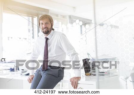 Portrait of smiling businessman wearing shirt and tie leaning on desk in office View Large Photo Image Stock Photo - Portrait of smiling businessman wearing shirt and tie leaning on desk in office. Fotosearch