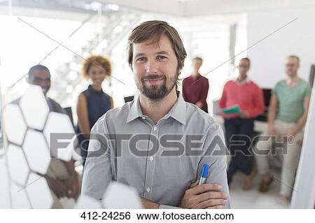 Stock Photograph - Portrait of smiling businessman wearing gray shirt, office team in background. Fotosearch