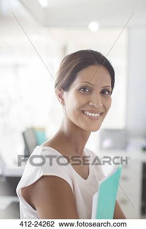 Stock Image - Portrait of smiling businesswoman holding documents in office. Fotosearch
