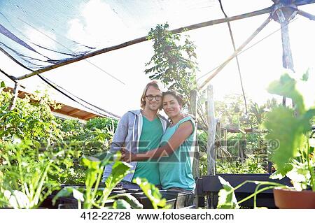 Portrait of smiling couple embracing in greenhouse, seedlings in foreground View Large Photo Image Stock Photo - Portrait of smiling couple embracing in greenhouse, seedlings in foreground. Fotosearch