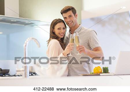 Portrait of smiling couple raising toast with champagne flutes in kitchen View Large Photo Image Stock Photo - Portrait of smiling couple raising toast with champagne flutes in kitchen. Fotosearch