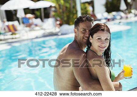 Portrait of smiling couple sitting by resort swimming pool View Large Photo Image Stock Photo - Portrait of smiling couple sitting by resort swimming pool. Fotosearch
